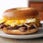 steak egg and cheese bagel sandwich served warm on a ceramic plate