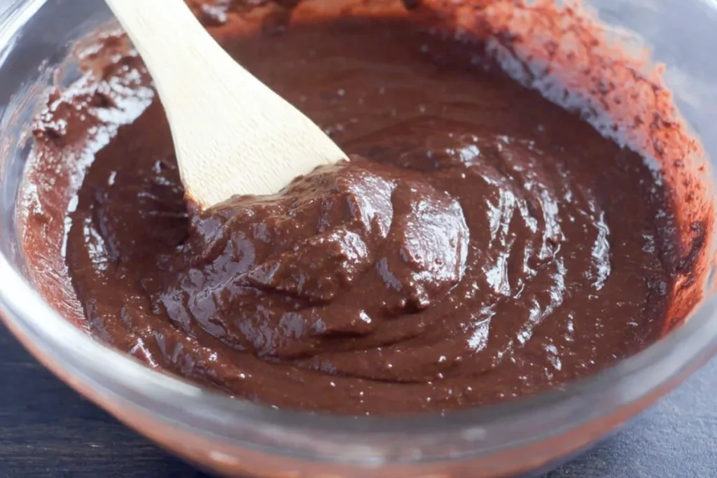 Glossy chocolate mixture for Turtle Texas Sheet Cake in a bowl with a wooden spoon