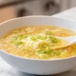 Photorealistic image of copycat egg drop soup with silky egg ribbons and green onions in a modern kitchen