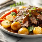 Crock Pot Pot Roast served with carrots, potatoes, and gravy on a white plate in natural daylight