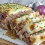 French onion meatloaf sliced with melted Gruyère and onion sauce on a plate