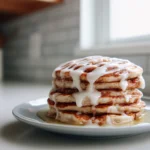 Fluffy Vegan Cinnamon Roll Pancakes That Taste Like a Cozy Morning Hug 11 stack of fluffy vegan cinnamon roll pancakes topped with vegan glaze in modern kitchen