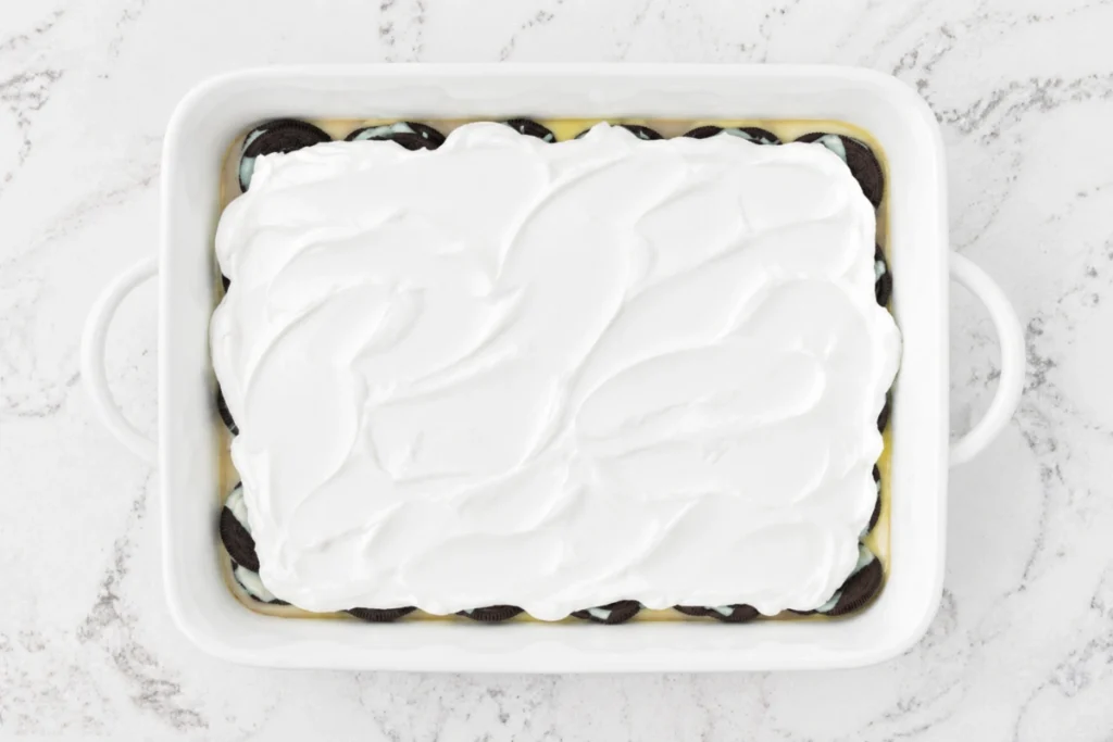 Oreo Dump Cake for an Easy Cookies-and-Cream Dessert 4 Oreo Dump Cake with whipped topping spread over the condensed milk layer