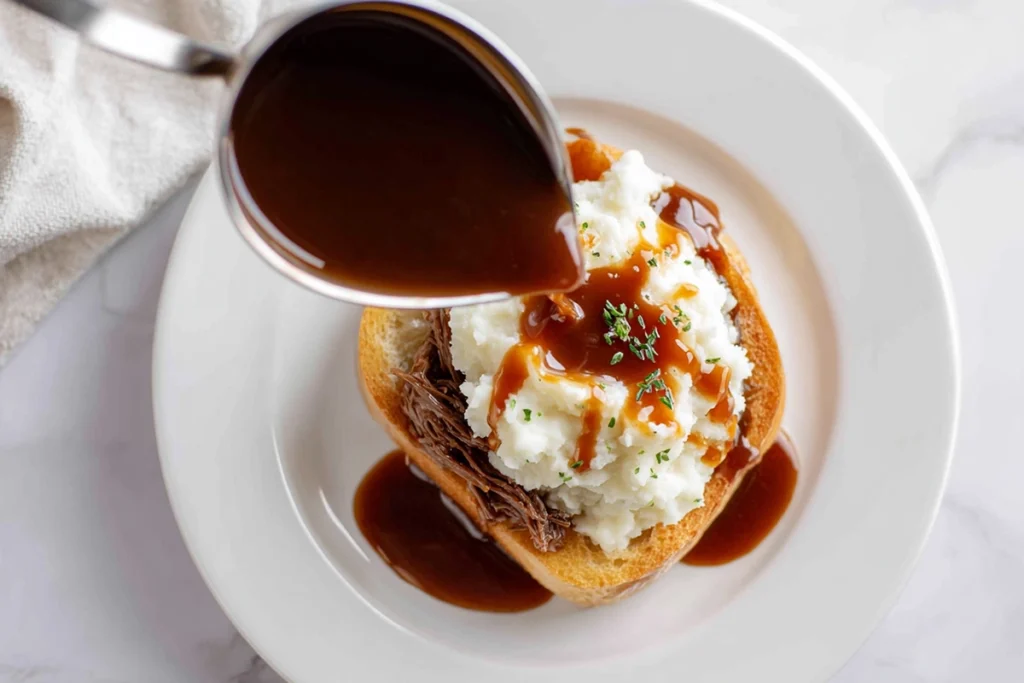 Slow Cooker Beef Manhattan – The Ultimate Comfort Food Classic Made Easy 10 Overhead view of plating Slow Cooker Beef Manhattan with gravy being poured over mashed potatoes and toast in a bright, modern kitchen.