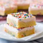 Soft and chewy sugar cookie bars with frosting and sprinkles on a marble counter