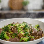 photorealistic beef and broccoli ramen stir fry in modern kitchen, glossy noodles and vibrant broccoli