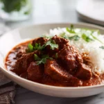 Photorealistic beef vindaloo curry in a white bowl with rice and cilantro garnish