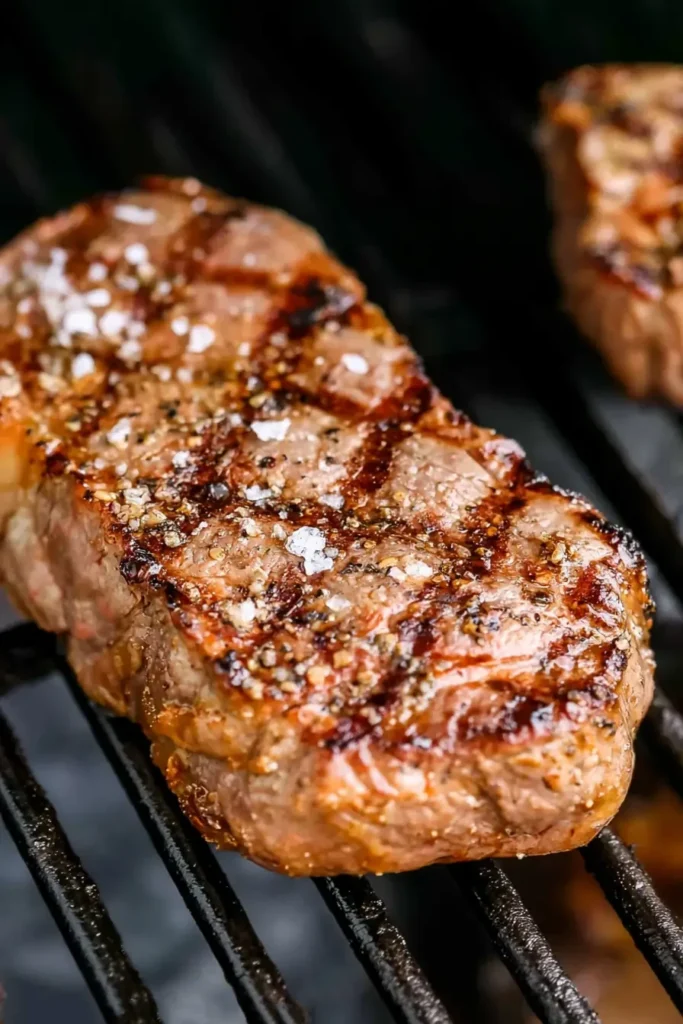 Rib eye steak grilling at medium heat with a browned seasoned crust