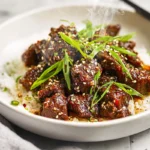 Slow Cooker Korean Beef plated with sauce, green onions, and sesame seeds