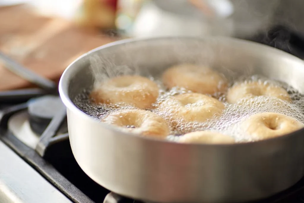 Bagels boiling in a stainless-steel pot during homemade bagel preparation in a modern kitchen