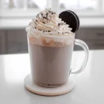 : Oreo Hot Chocolate topped with whipped cream and crushed Oreos in a modern kitchen