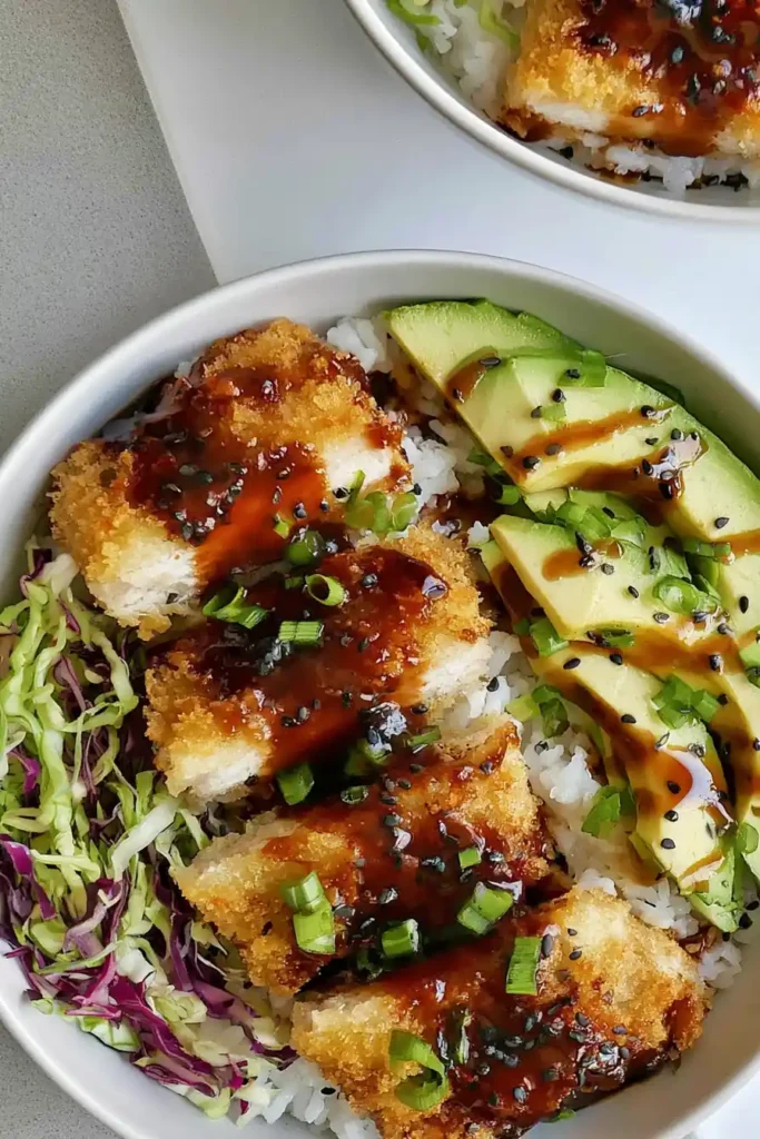 Japanese Katsu Bowls with Crispy Sheet-Pan Chicken 3 Japanese Katsu Bowls assembled with sliced sheet-pan chicken, warm rice, dressed slaw, avocado, and tonkatsu sauce