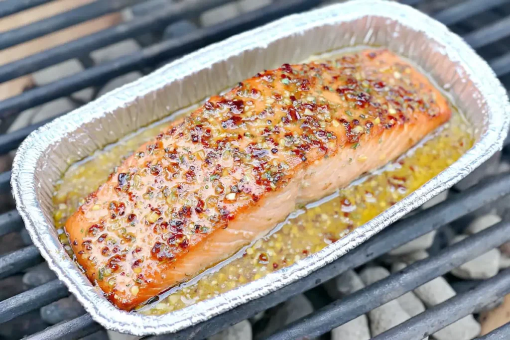 salmon cooking in foil tray on grill with bubbling marinade