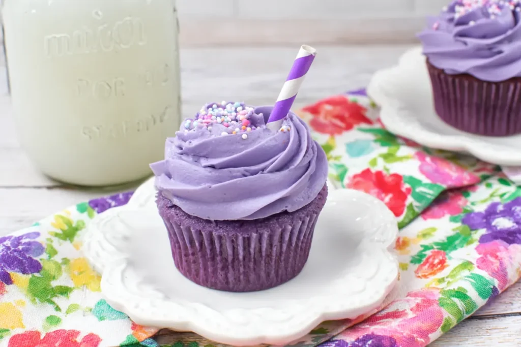 Single grape soda cupcake with purple frosting on a white plate with floral cloth