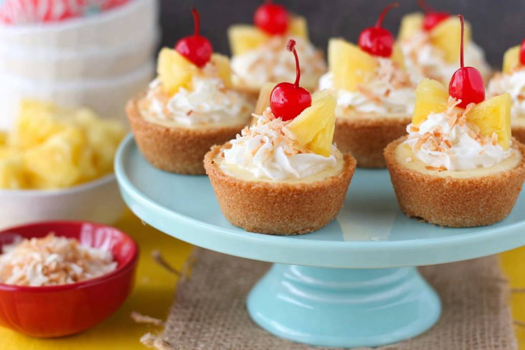 Pina Colada Cookie Cups topped with whipped cream, pineapple, and cherries on a pale blue cake stand