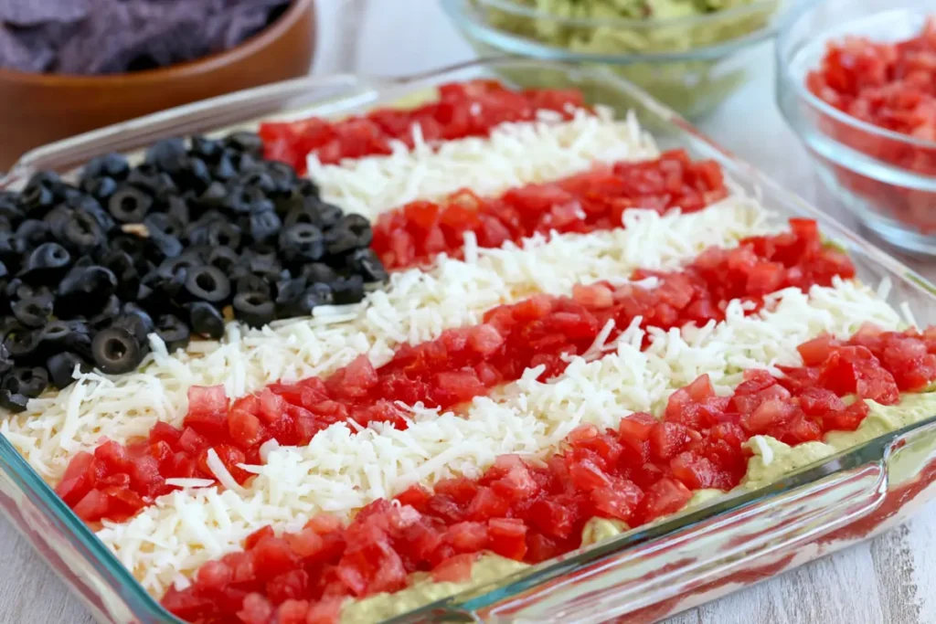 Black olive stars on American flag layered taco dip with tomato and cheese stripes